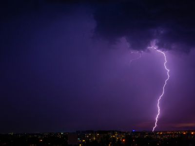 Lightning striking during a storm over a city skyline, highlighting the potential for power outages and the importance of standby generators for home protection.