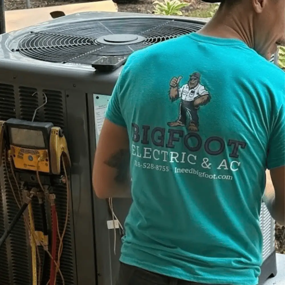 Technician in blue Bigfoot Electric & AC shirt working on HVAC unit, showcasing expert service in Central Louisiana.