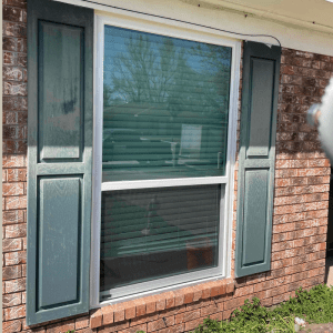 Energy-efficient replacement window with green shutters and brick exterior, showcasing modern design and functionality for improved comfort and performance.