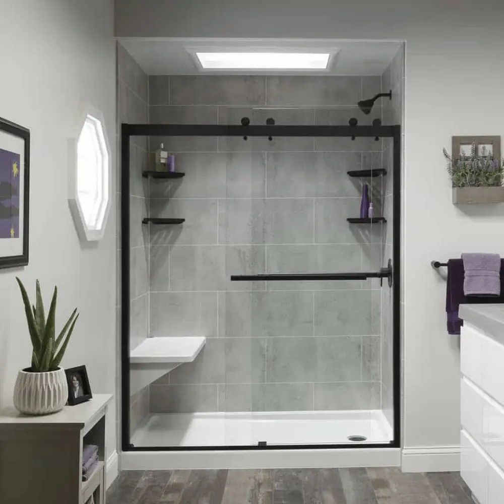 Walk-in shower with modern design, featuring gray tile walls, black fixtures, built-in shelves, and a sleek glass door, showcasing bathroom renovation potential by Bigfoot Electric & AC.