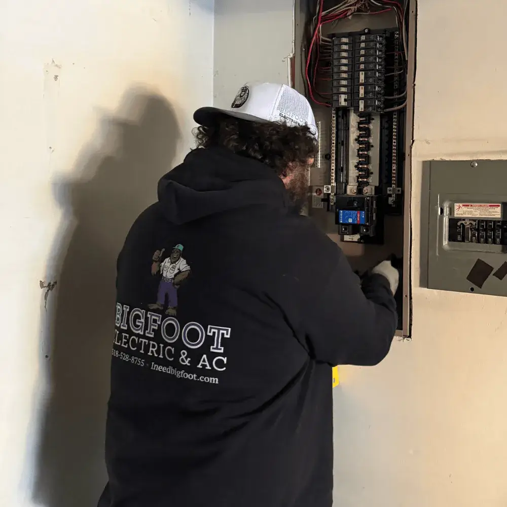 Electrician in Bigfoot Electric & AC hoodie working on electrical panel, demonstrating licensed electrical service in Pineville, LA.